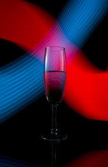 A single wine glass isolated on a black background with red white pink and orange neon light painting streaks of light behind them. Light wave, game of colors, drawing light.