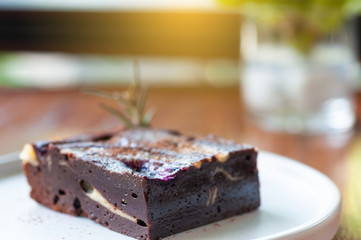 Square chocolate brownie in white plate on wooden table.
