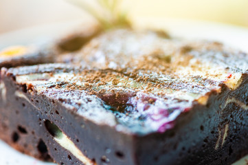 Square chocolate brownie in white plate on wooden table.