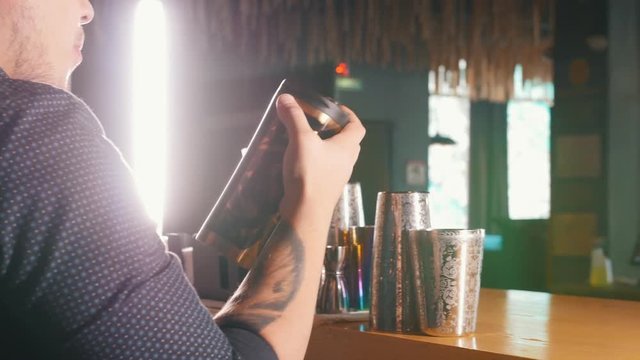 Young professional bartender drinks from a painted shaker, and continues to mix cocktail