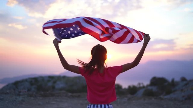 Child girl is running with USA American flag at sunset. Slow motion