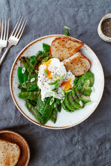 Top view of healthy breakfast or lunch. Fried snow peas, avocado, poached eggs are sprinkled chia seeds with toasts.