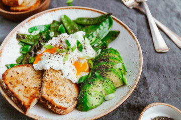 Healthy breakfast or lunch. Fried snow peas, avocado, poached eggs are sprinkled chia seeds with toasts.