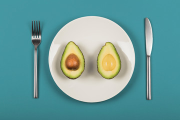 Avocado halves on a white plate with knife and fork