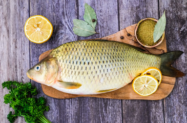 Carp on a wooden kitchen Board surrounded by lemons, spices, greens. Fish ready to cook.