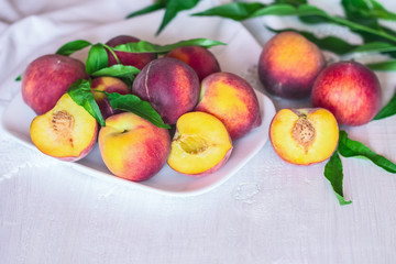 Fototapeta na wymiar whole peaches and halves of peaches in a white plate on the table close-up. background with peaches, peach halves and leaves.