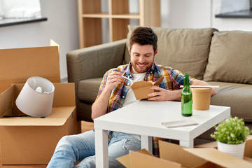 moving, consumption and people concept - smiling man eating takeaway food for lunch at new home