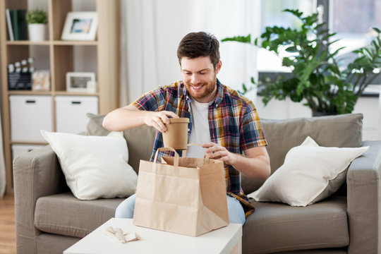 consumption, eating and people concept - smiling man unpacking takeaway food at home