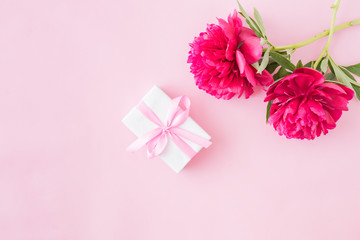 Flat lay composition with red peonies and gift box on a pink background