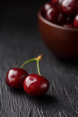 Ripe and juicy cherry berries on a black textural background in a brown cup, with water drops. Top view, close-up.