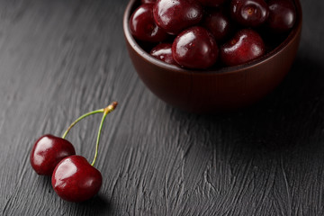 Ripe and juicy cherry berries on a black textural background in a brown cup, with water drops. Top view, close-up.