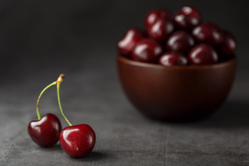 Ripe and juicy cherry berries on a black textural background in a brown cup, with water drops. Top view, close-up.