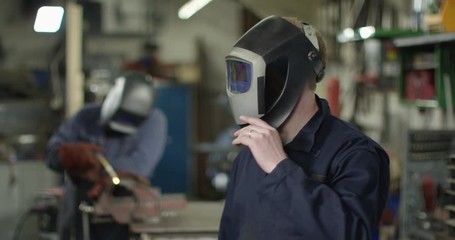 4K Mechanic in garage workshop lifting his welding visor & looking at camera. Slow motion.