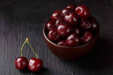 Ripe and juicy cherry berries on a black textural background in a brown cup, with water drops. Top view, close-up.