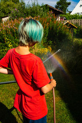 Boy watering garden with hose causes rainboy with the spray