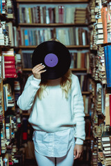 Obraz premium young adult woman in white sweater holding vinyl in library