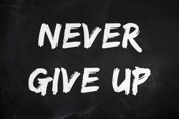 The motivational words Never Give Up, written with chalk on a rough worn blackboard surface.