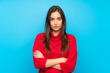 Young woman with red sweater over isolated blue background keeping arms crossed