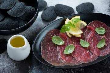 Close-up of carpaccio beef with black potato chips, fresh green basil, lemon and olive oil,...