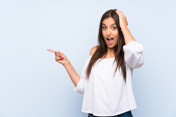 Young woman over isolated blue background surprised and pointing finger to the side