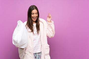 Young woman in pajamas and dressing gown over isolated purple background laughing