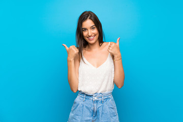 Young woman over isolated blue background with thumbs up gesture and smiling
