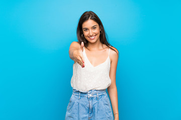 Young woman over isolated blue background shaking hands for closing a good deal