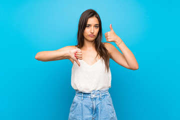 Fototapeta na wymiar Young woman over isolated blue background making good-bad sign. Undecided between yes or not