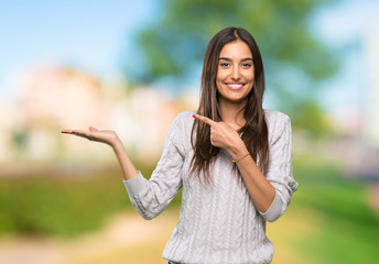 Young hispanic brunette woman holding copyspace imaginary on the palm to insert an ad at outdoors