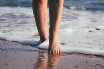 Female legs in the water. The girl goes along the coastline. Sunset light and sea foam.