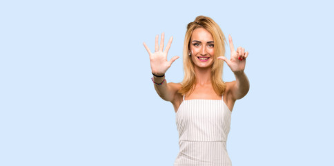 Young blonde woman counting seven with fingers over isolated blue background