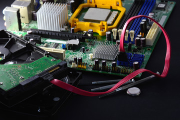 Computer hard disks lie on a black matte background among screwdrivers for repair. The motherboard...
