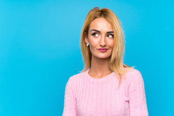 Young blonde woman over blue background standing and looking to the side
