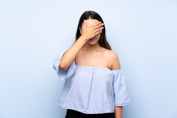Young brunette woman over isolated blue background covering eyes by hands