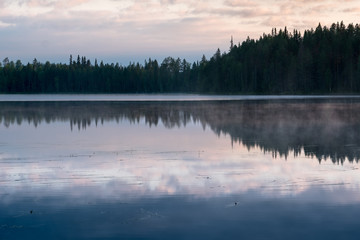 Obraz na płótnie Canvas Misty Sunrise over a finnish lake in dark forest with beautiful reflections, Kainuu, Finland