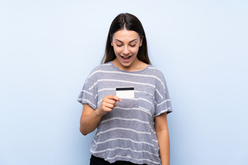 Young brunette woman over isolated blue background holding a credit card