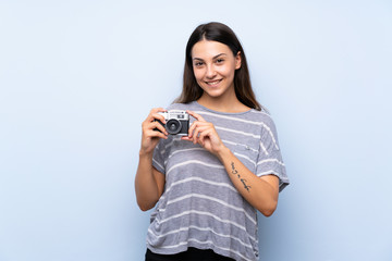 Young brunette woman over isolated blue background holding a camera