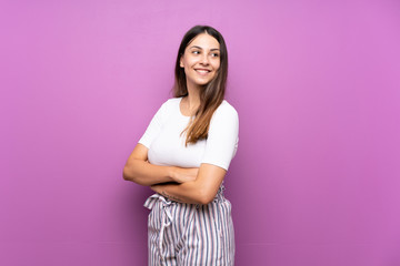 Fototapeta premium Young woman over isolated purple background with arms crossed and happy