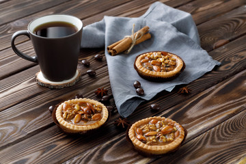 Mini tarts with nuts and honey next to a mug of tea on a wooden background