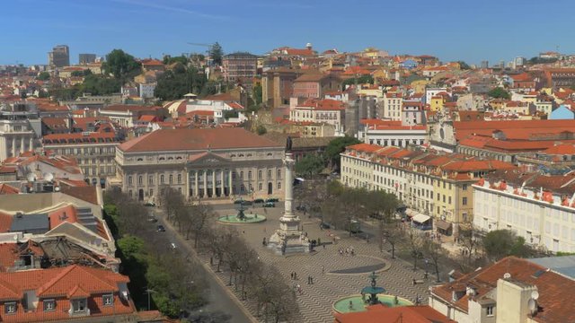 A top view of a Rossio square on a beautiful sunny day with busy everyday life happening on it. People going in different directions, cars driving along the square. There is a colorful urban view