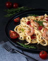 Close-up of pasta in cream sauce with shrimps, cherry tomato and arugula on dark background