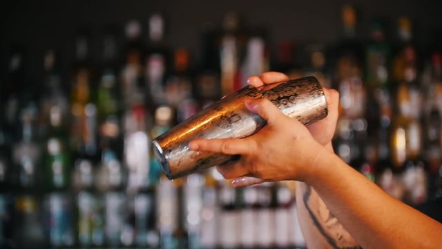 Professional young barman using a pair of glasses prevents cocktail