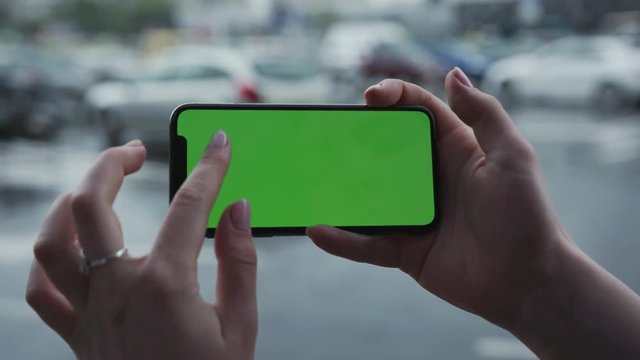 Los Angeles, California - 5 April 2019: Close up view woman hand holding horizontal smart phone cellphone with green screen background rain parking cars weather cellphone outside rain trees raindrops