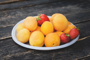 Apricot and strawberry in plate on the old wooden table.