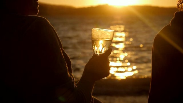 Silhouette of two women sitting on shore of Mediterranean sea, drinking an alcoholic drink at sunset. Greece. Slow motion. HD
