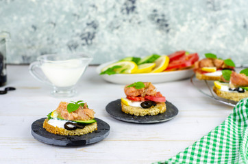 small canape with pink salmon fish, cucumber, tomato, olive and lemon on a light wooden background