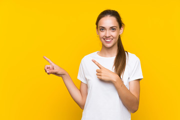 Young woman over isolated yellow background pointing finger to the side