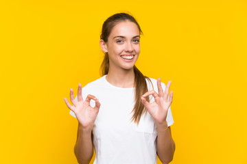 Young woman over isolated yellow background showing an ok sign with fingers