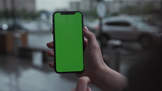 Los Angeles, California - 5 April 2019: Hands woman holding use touch vertically smart phone cellphone with green screen background rain parking cars weather app cellphone outside rain trees raindrops