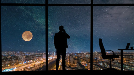 The man phones near the panoramic window on city with starry sky background